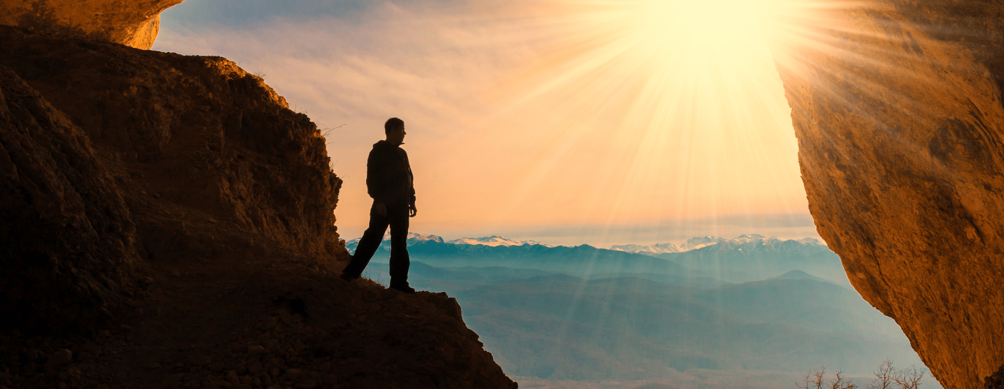 man on cliff looking at sun rays